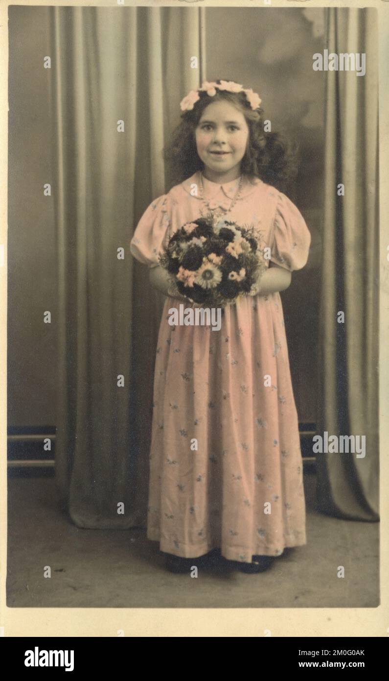 Une jeune fille (8-10 ans) habillée comme demoiselle d'honneur, se tenait dans un studio de photographes, avec une grande posie de fleurs. Photo prise 2 janvier 1940. L'impression a été professionnellement colorée à la main par le studio, Jeromes, qui a dirigé une chaîne de studios photographiques de grande rue à budget à travers la Grande-Bretagne. Banque D'Images