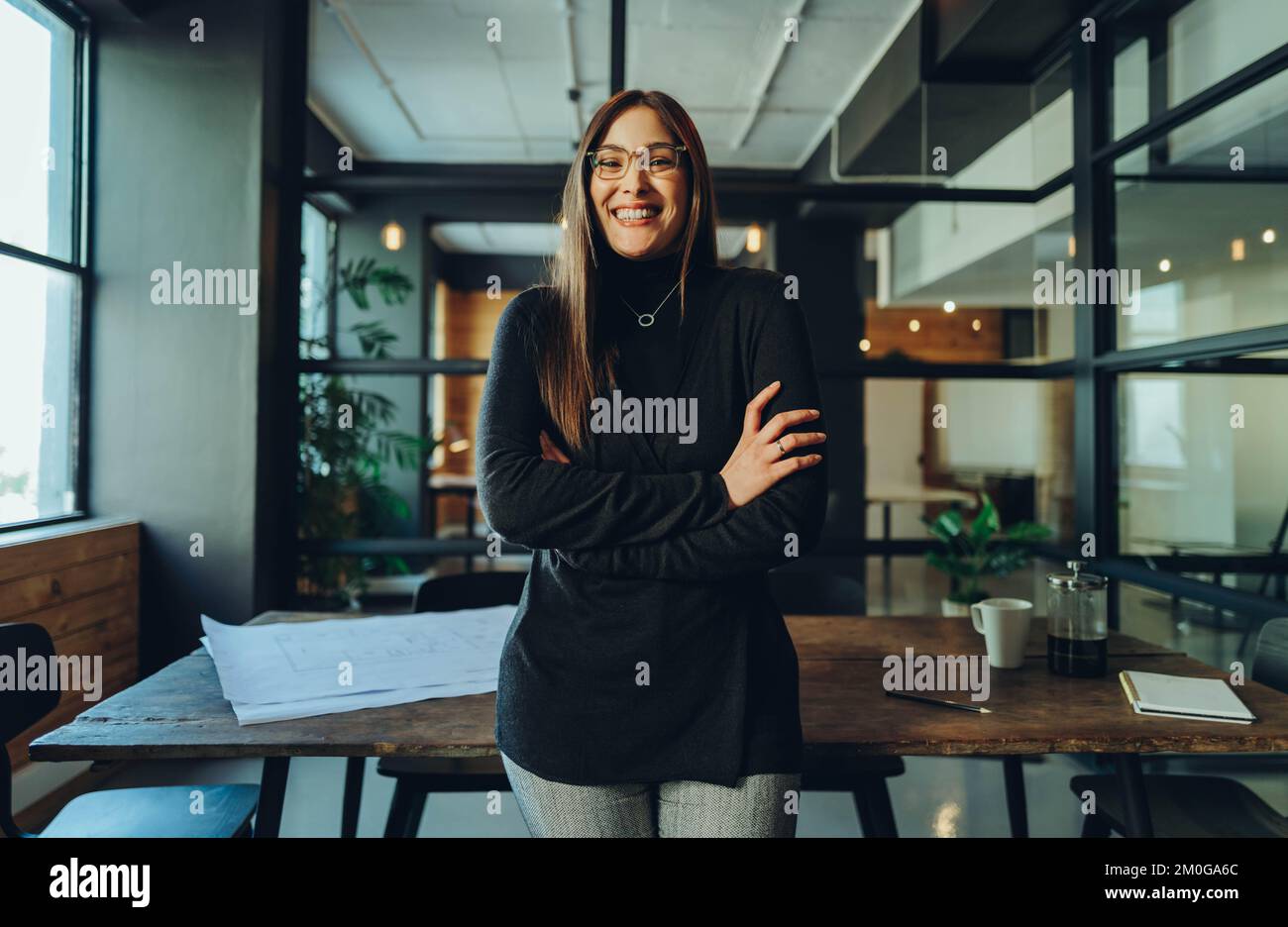 Femme professionnelle souriant à la caméra tout en se tenant debout avec ses bras croisés. Jeune femme d'affaires gaie debout dans la salle de réunion d'un M. Banque D'Images