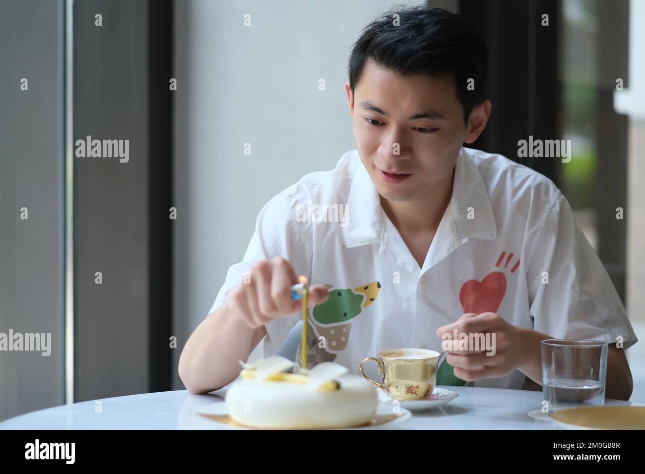 Un jeune homme asiatique allume la bougie sur un gâteau d'anniversaire Banque D'Images