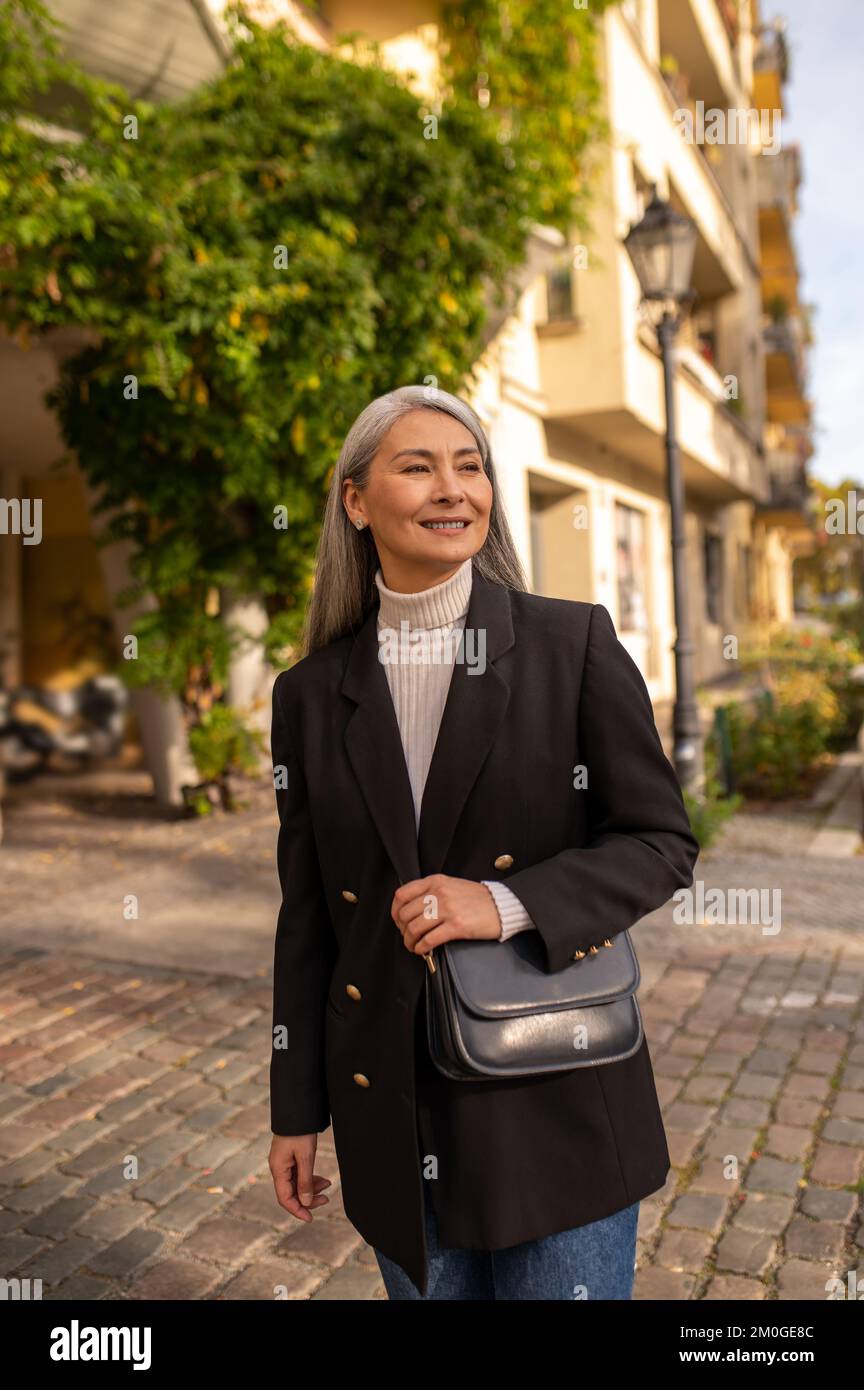 Une jolie femme souriante dans un manteau noir dans la rue de la ville Banque D'Images