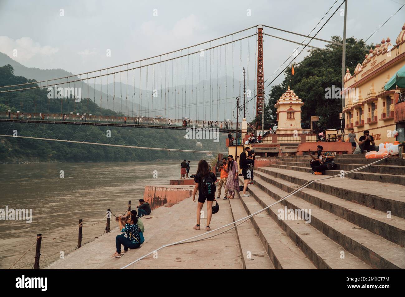 Une belle photo de personnes assises près du Gange avec le pont RAM Jhula en arrière-plan Banque D'Images