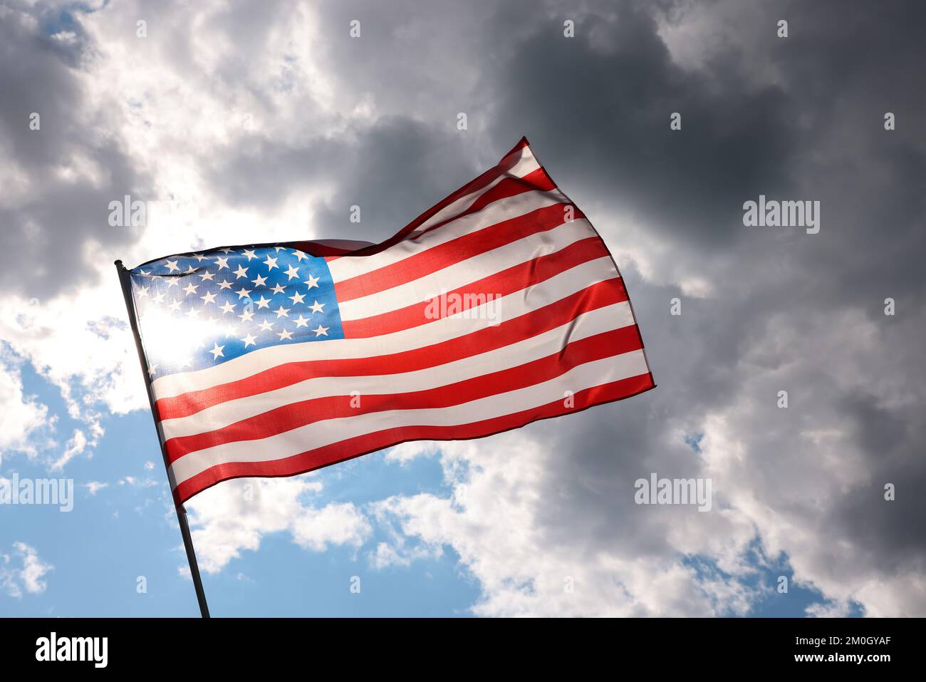 Drapeau national américain rétroéclairé volant et agitant dans le vent au-dessus d'un ciel nuageux gris orageux, symbole du patriotisme américain, angle bas, vue latérale Banque D'Images
