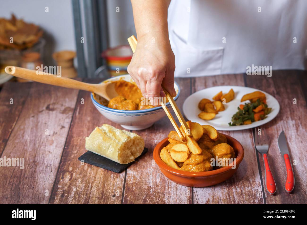 femme méconnaissable en tablier blanc servant des pommes de terre et des légumes sur une portion de boulettes de viande dans un plat en faïence Banque D'Images