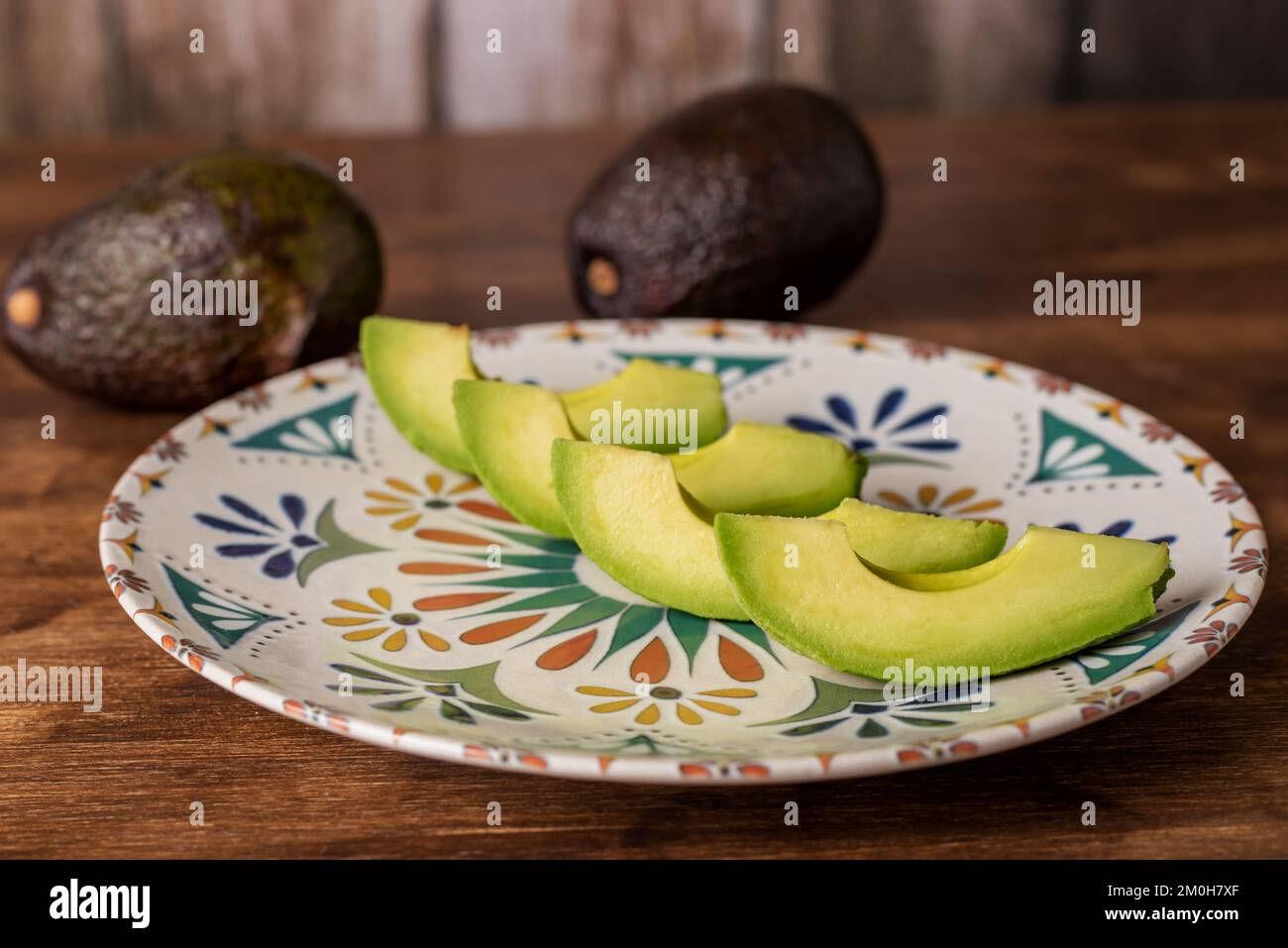 Morceaux d'avocat sur une plaque rustique sur une table en bois accompagnés de plus d'avocats. Banque D'Images