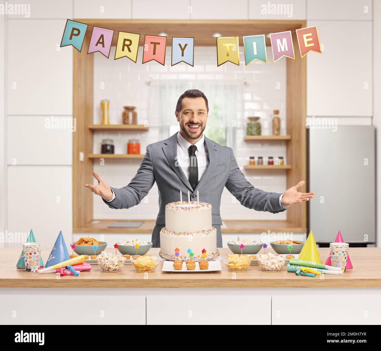 Jeune homme se préparant pour une fête et posant dans une cuisine avec un gâteau et des faveurs de fête sur un comptoir Banque D'Images