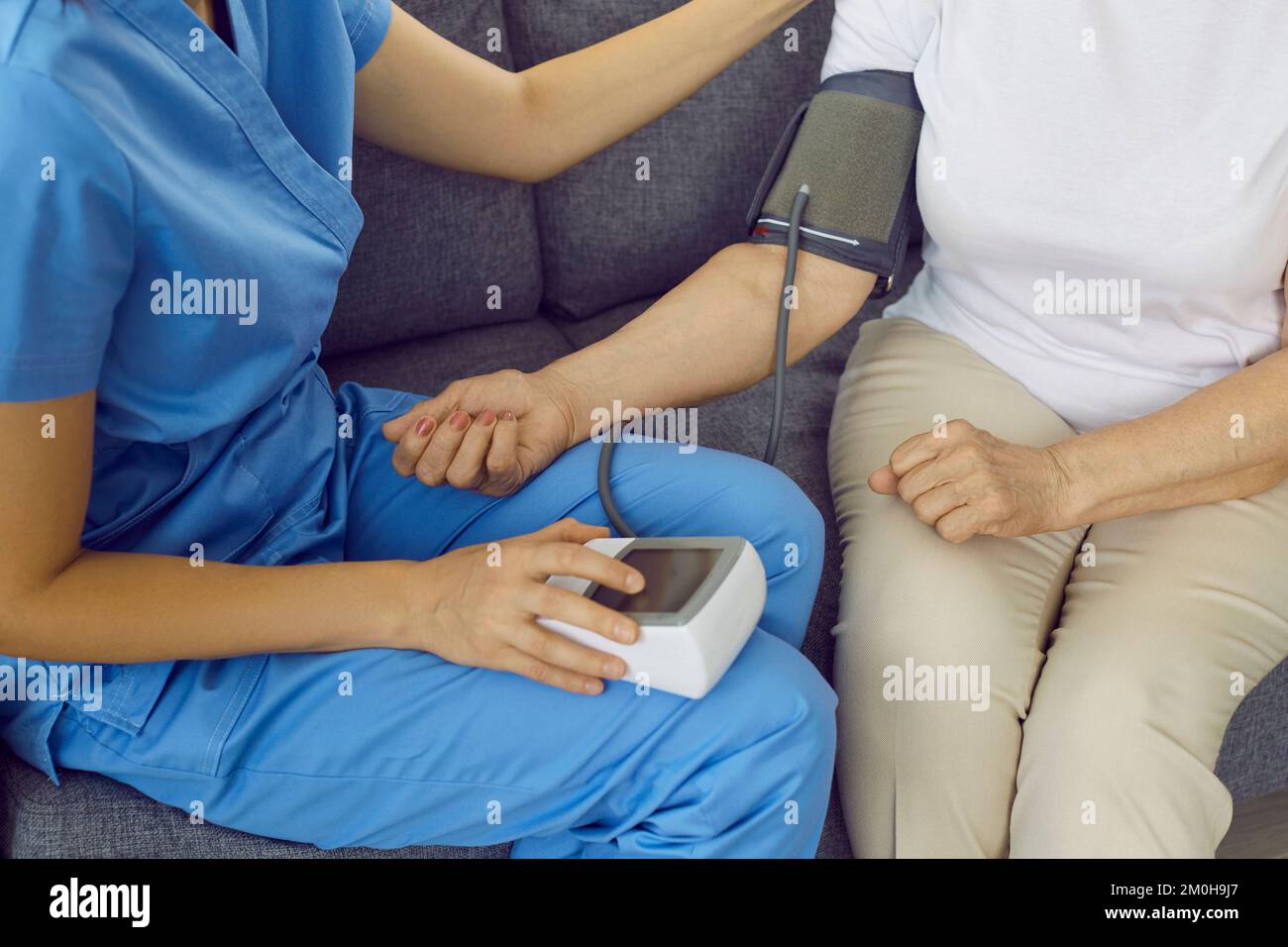 Médecin assis sur le canapé et mesurant la pression artérielle d'un patient âgé souffrant d'hypertension Banque D'Images