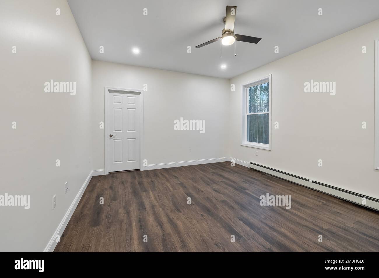 L'intérieur d'une pièce avec parquet, une plinthe chauffante sur le mur blanc et un ventilateur de plafond Banque D'Images