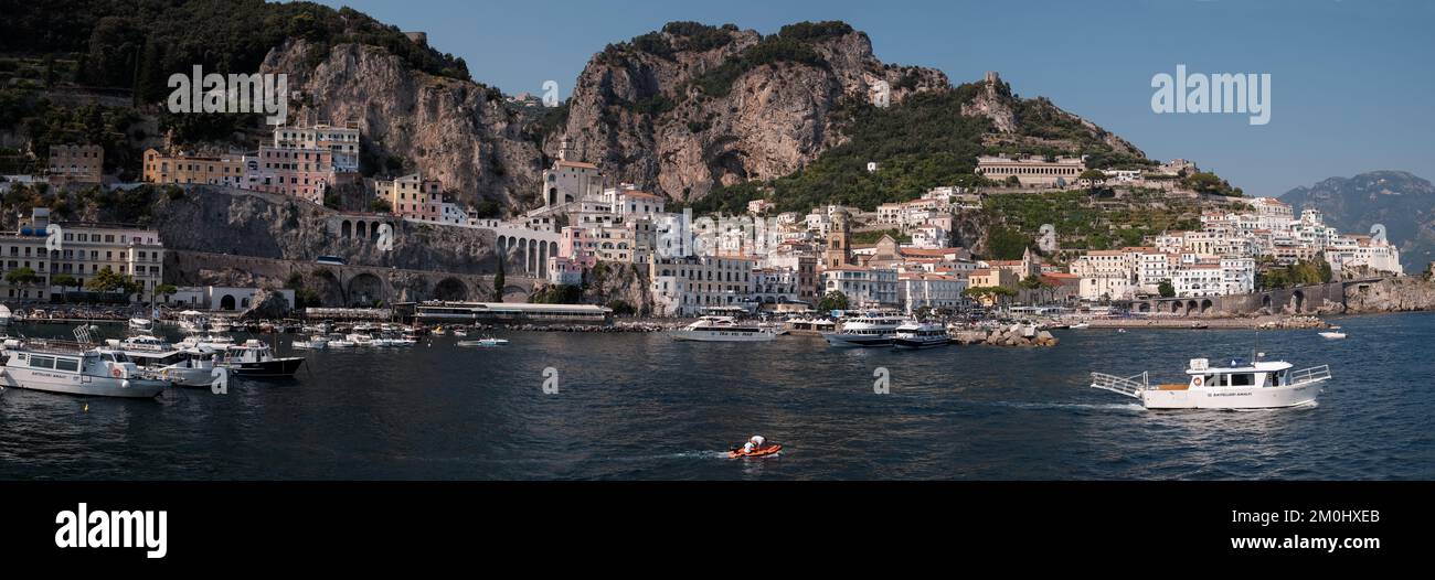 Panorama de la ville d'Amalfi depuis le port de plaisance en direction de la ville principale avec des yachts à moteur de luxe en premier plan et des falaises pittoresques en arrière-plan. Banque D'Images