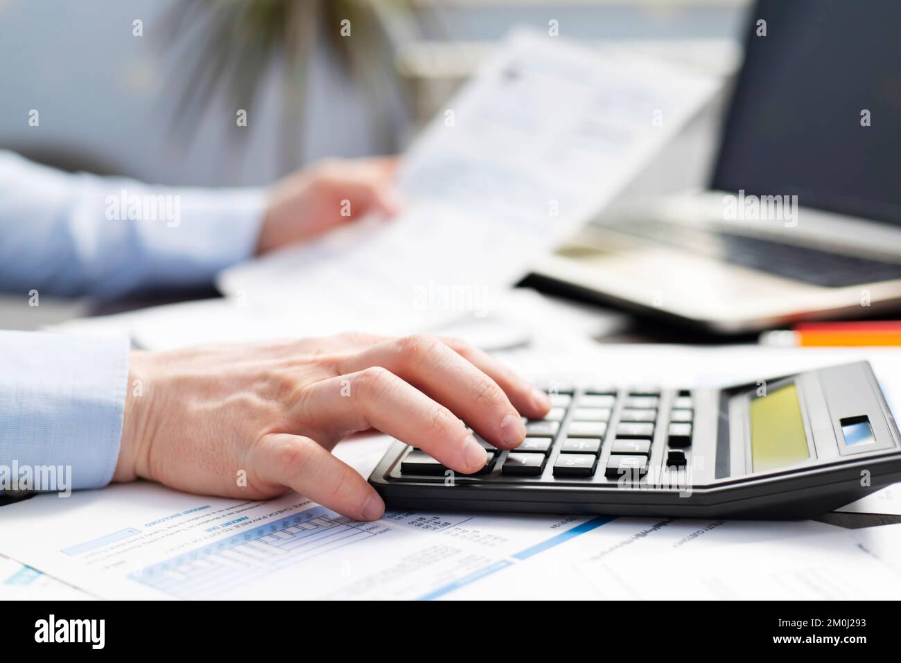Homme d'affaires utilisant la calculatrice pour calculer les factures à la table dans le bureau Banque D'Images