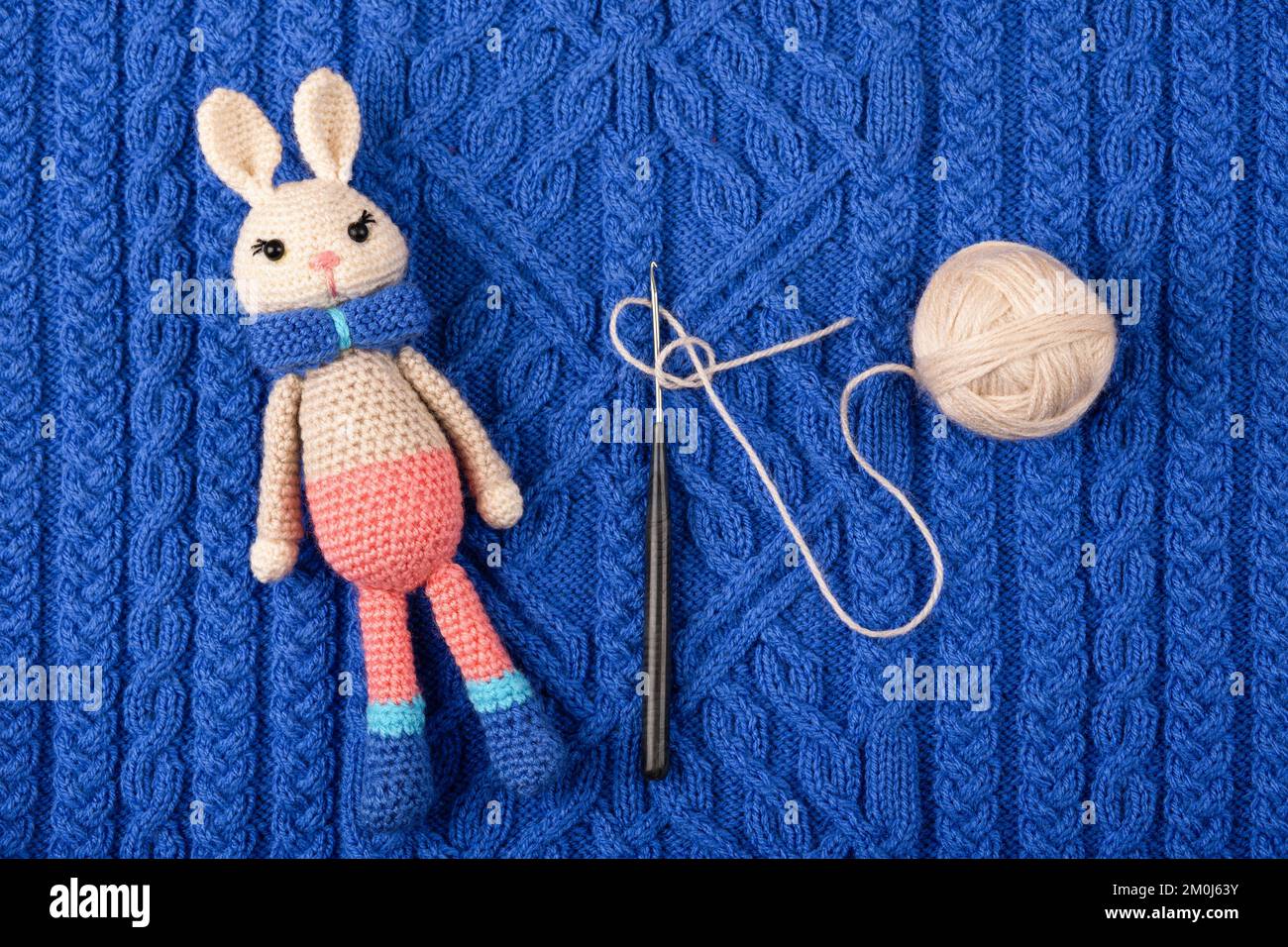 Un jouet en bonneterie lièvre ou lapin avec une boule de fil et un crochet en crochet sur un tissu bleu tricoté. Le symbole de 2023. Banque D'Images