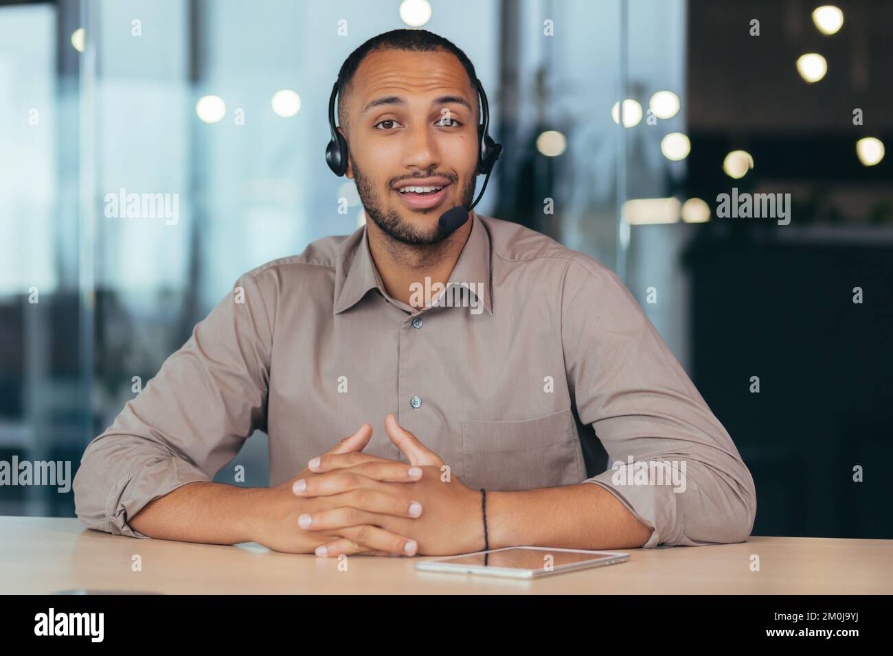 Portrait d'un jeune homme afro-américain élégant. Il est assis dans un micro-casque devant la caméra, parle, consulte. Formation professionnelle, webinaire, service d'assistance clientèle, boutique en ligne. Banque D'Images