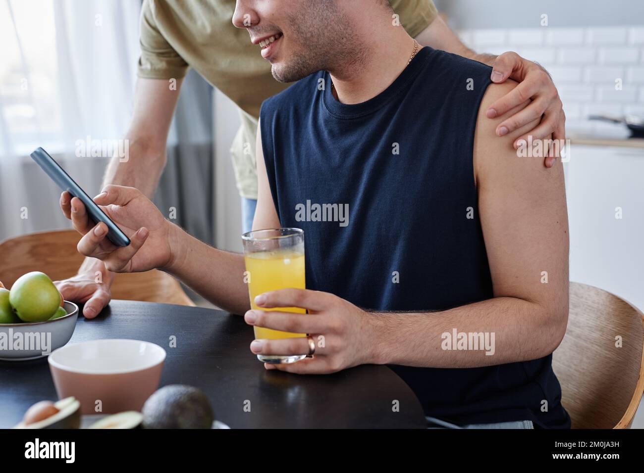 Vue latérale gros plan de jeunes couples gays prenant le petit déjeuner le matin et tenant un smartphone Banque D'Images