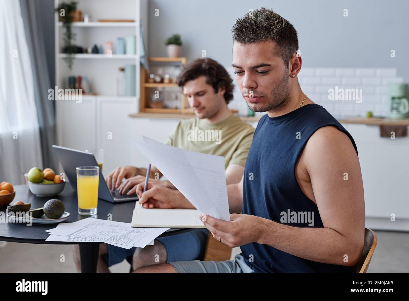 Portrait du jeune couple gay vivant ensemble avec l'accent sur l'homme étudiant à la table de cuisine Banque D'Images