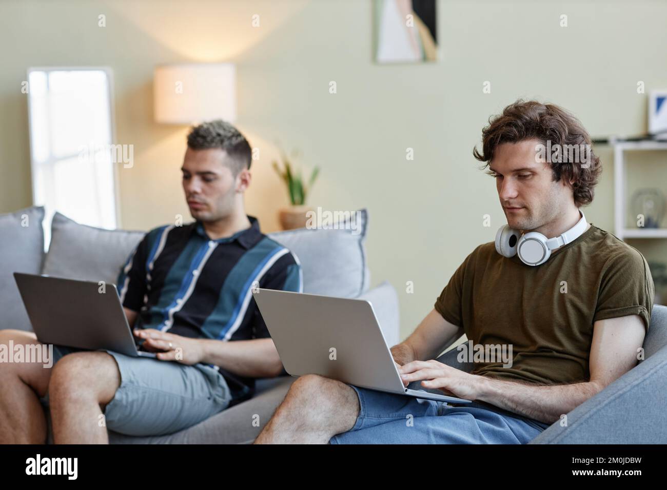 Portrait de deux jeunes hommes vivant ensemble et utilisant des ordinateurs travaillant à domicile Banque D'Images