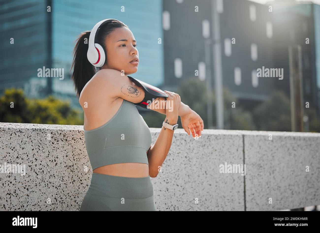 Jeune femme de fitness portant un casque et écoutant de la musique tout en s'étirant avant une course à l'extérieur de la ville. L'exercice est bon pour la santé et Banque D'Images
