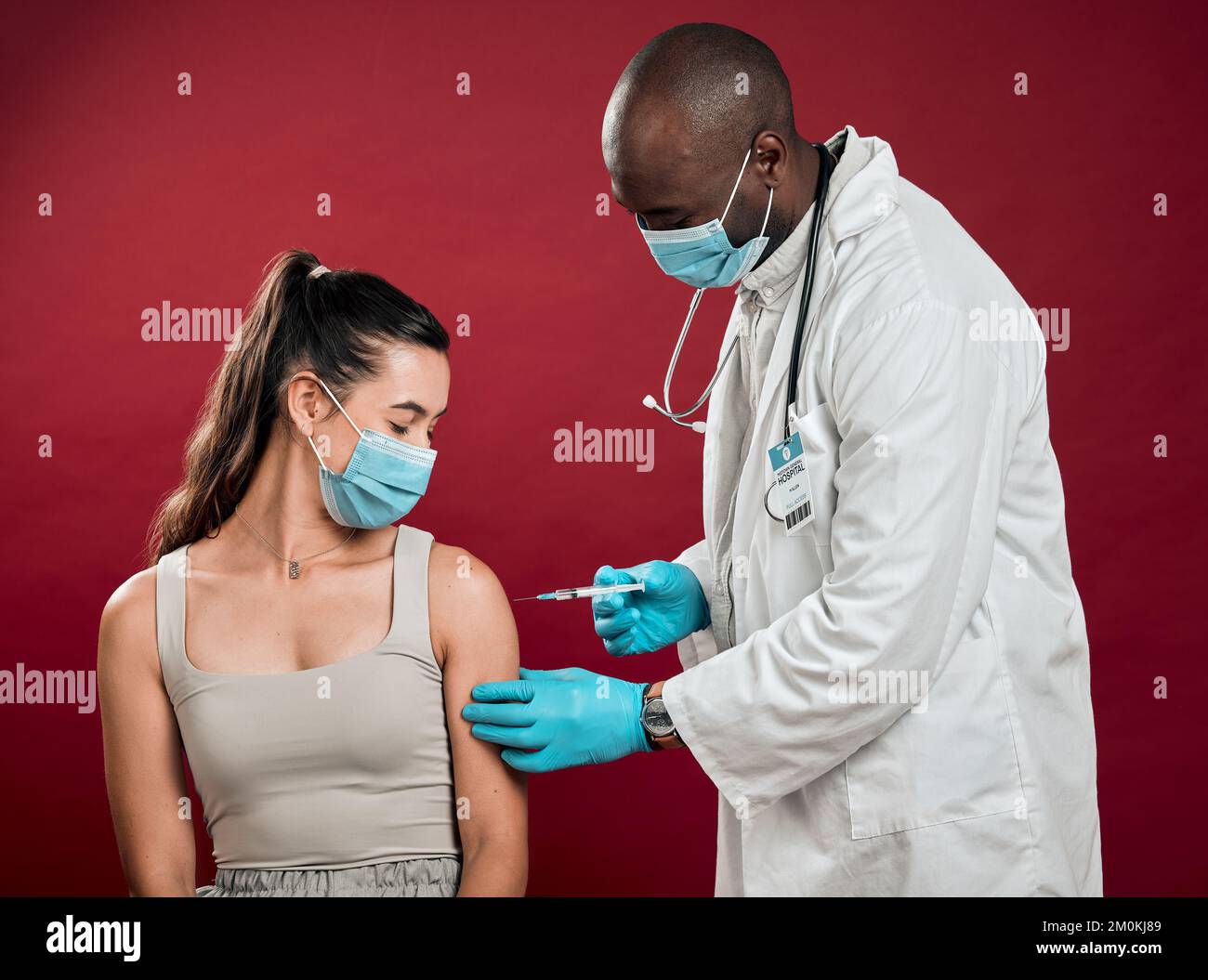 Médecin afro-américain qui donne le vaccin contre le covid à une femme de race mixte et qui porte un masque chirurgical. Patient hispanique ayant obtenu une injection de corona de Banque D'Images