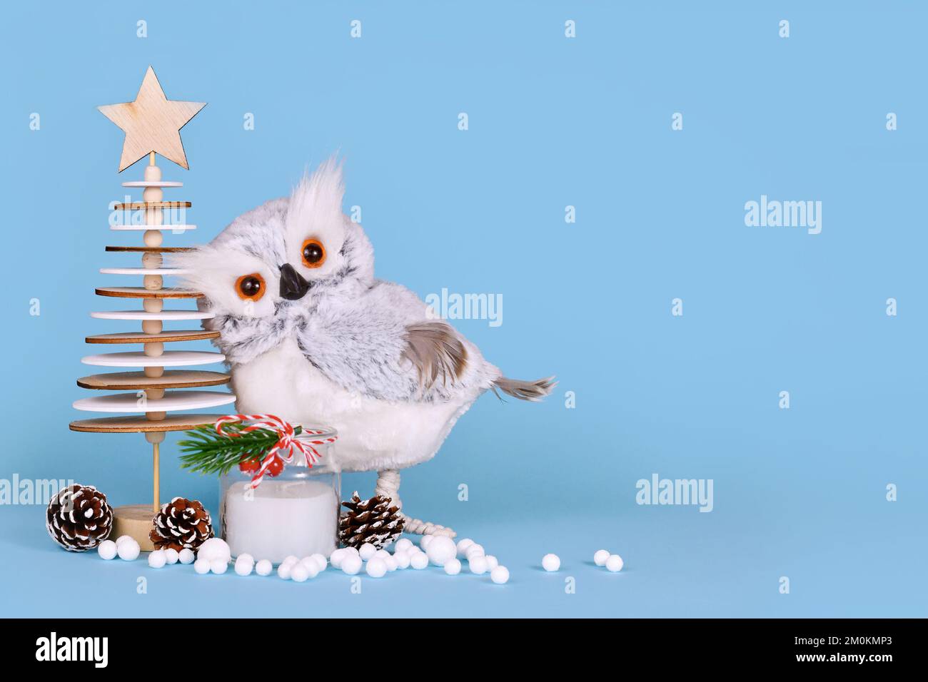 Décoration de Noël de saison avec hibou enneigé, arbre en bois, bougie, cônes de pin et boules de neige sur fond bleu avec espace de copie Banque D'Images