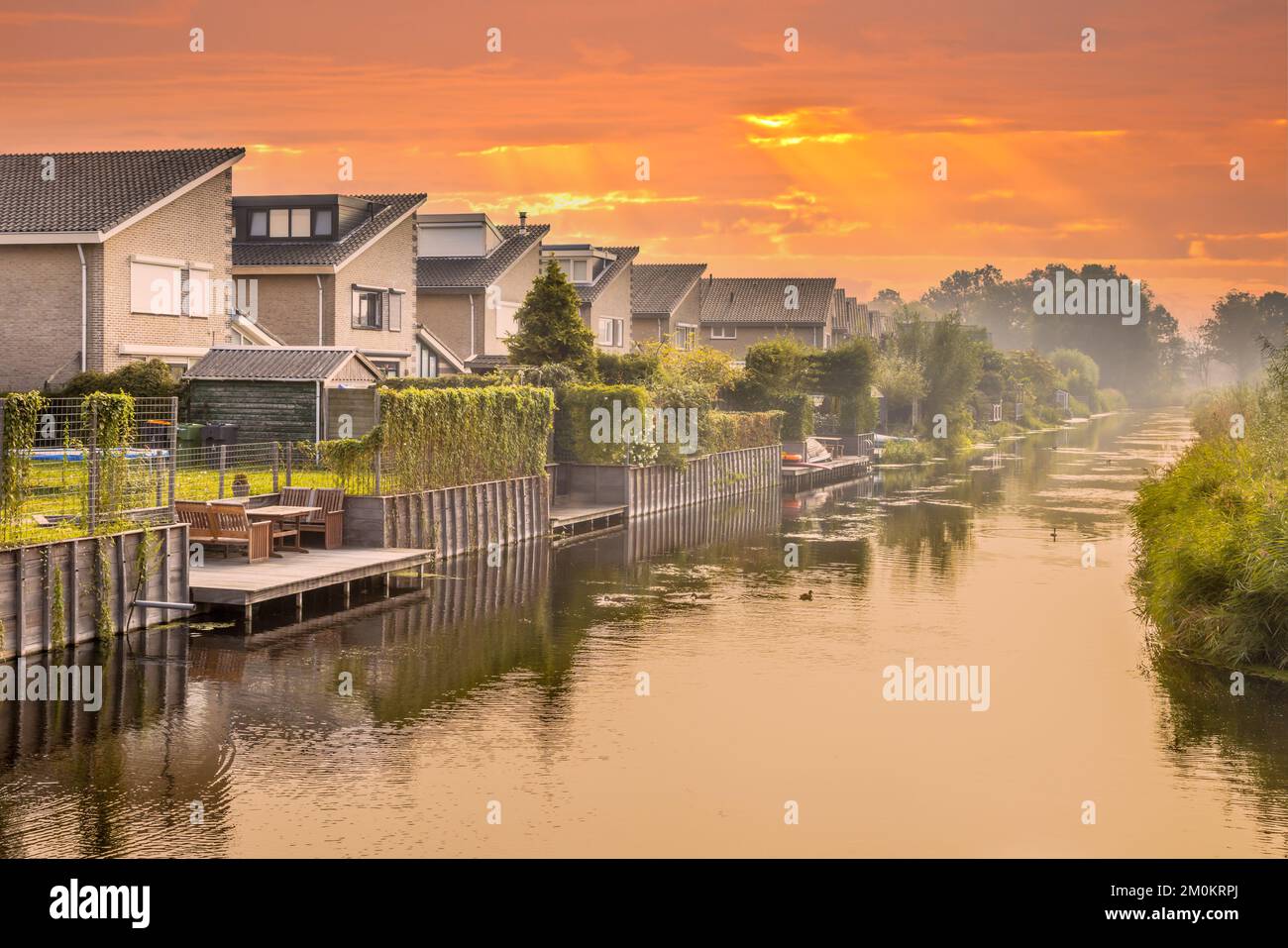 Maisons au bord de l'eau dans la zone résidentielle aux pays-Bas. Sous le ciel orange. Banque D'Images