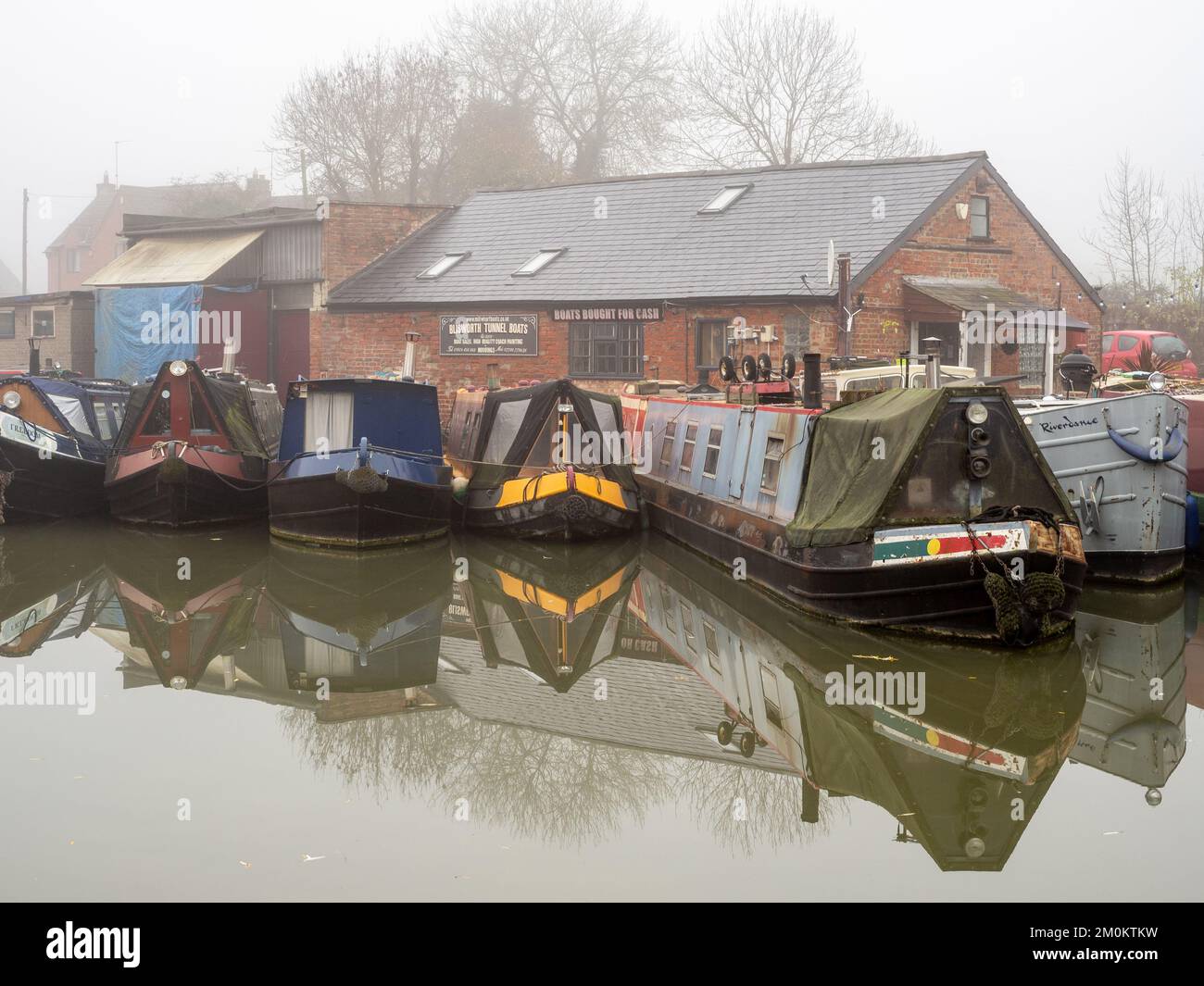 Un matin d'hiver froid et brumeux sur le canal de Grand Union, Blisworth, Northamptonshire, Royaume-Uni; avec des bateaux étroits amarrés à l'extérieur d'une cour de bateaux Banque D'Images