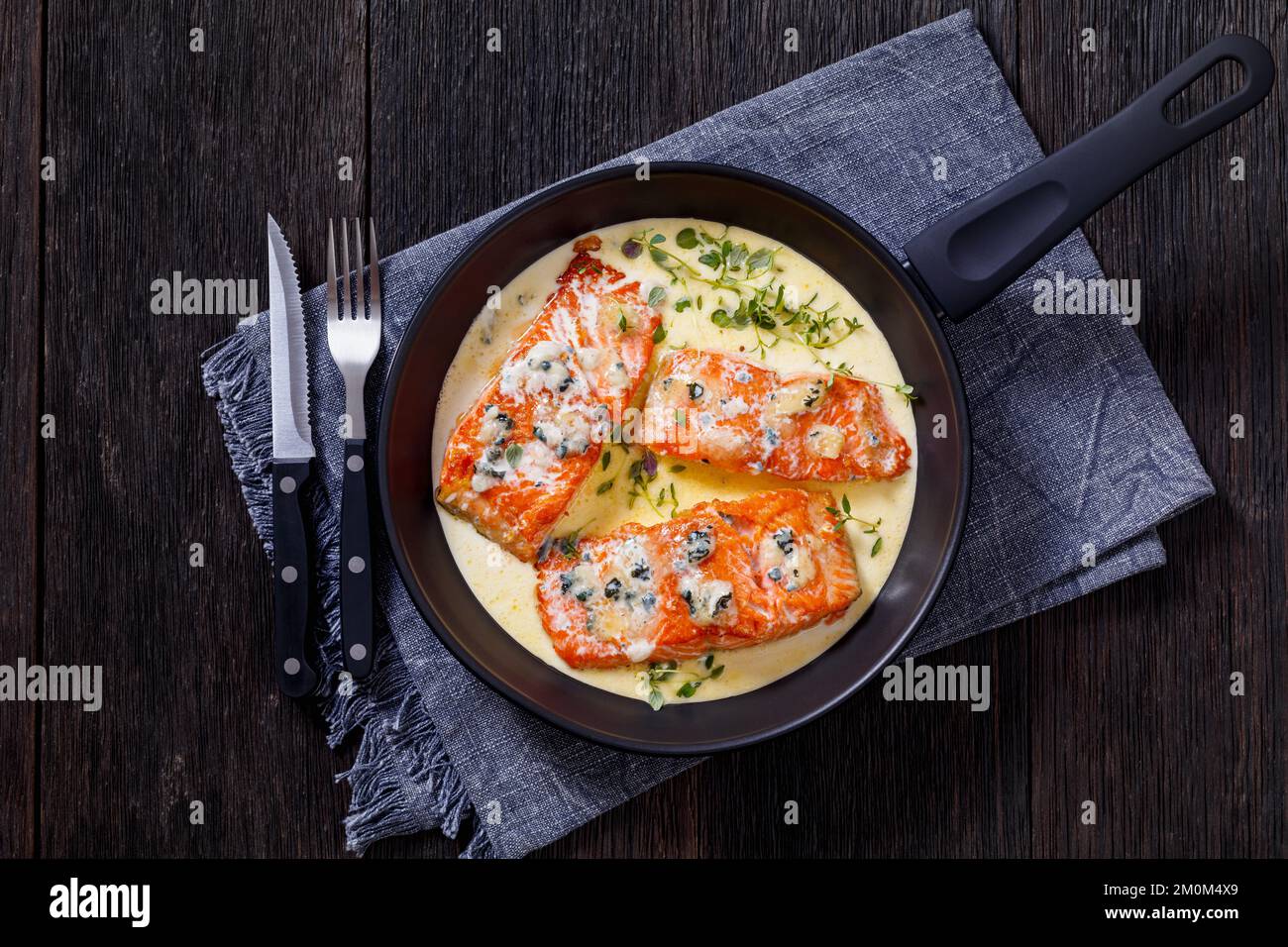 filet de saumon cuit avec une sauce crémeuse au fromage bleu moule dans une casserole sur une table en bois sombre avec couverts, vue horizontale depuis le dessus, plat Banque D'Images