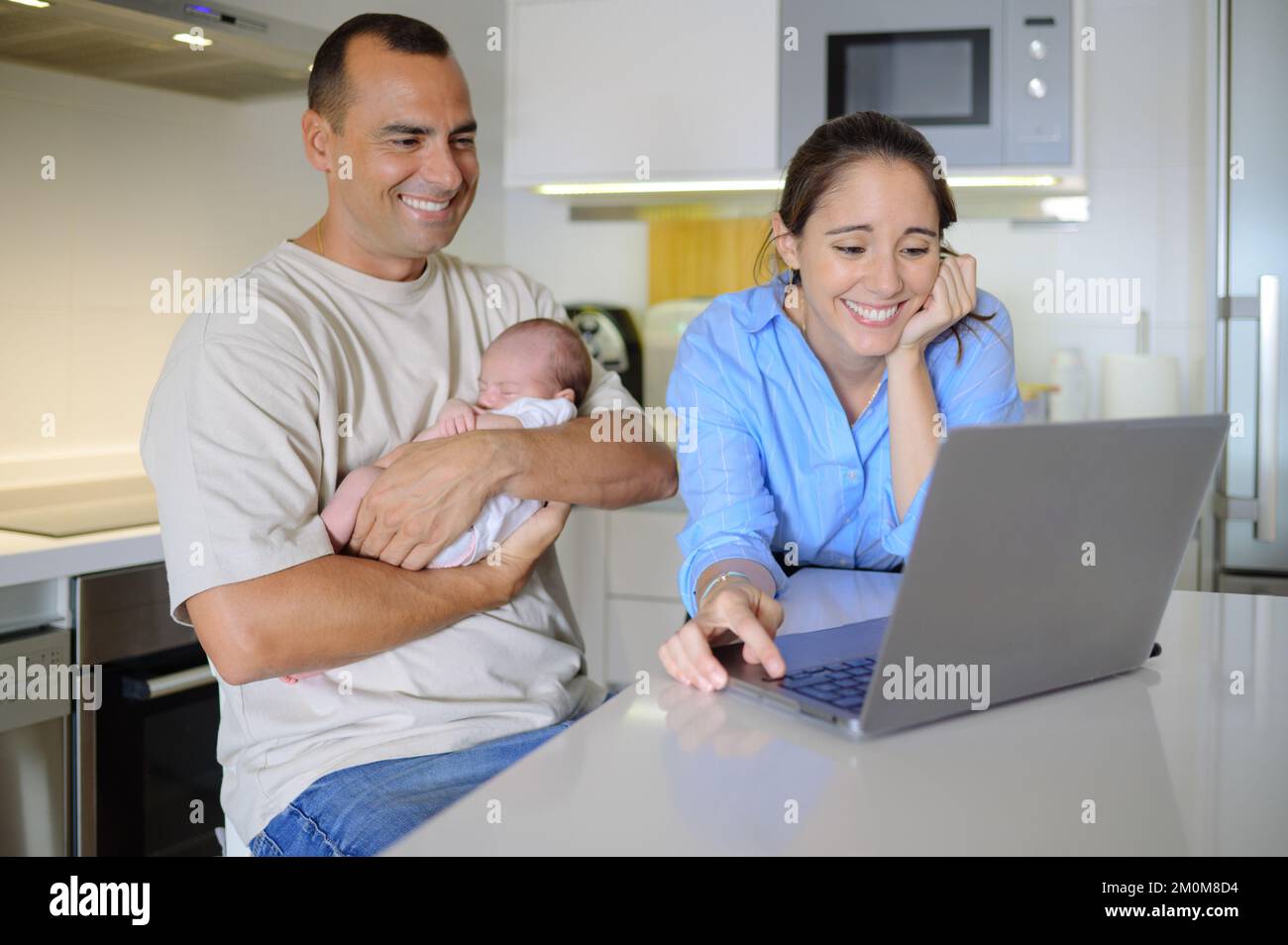Mère et père sensuels avec bébé endormi regardant des photos sur ordinateur portable Banque D'Images