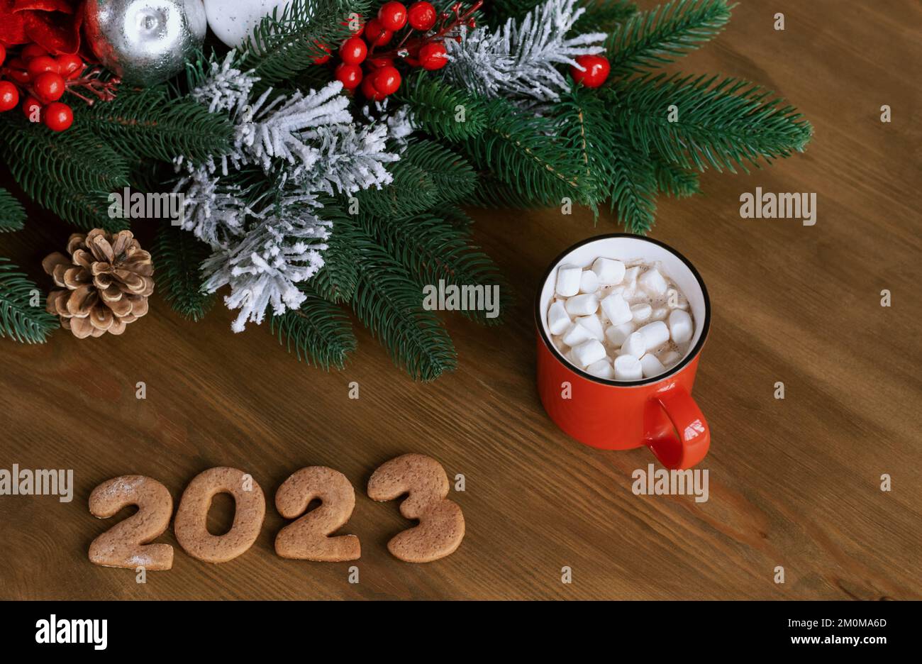 Tasse rouge, mug avec guimauve, biscuits au pain d'épice en forme de 2023 ans et décoration de sapin de Noël sur table en bois Banque D'Images