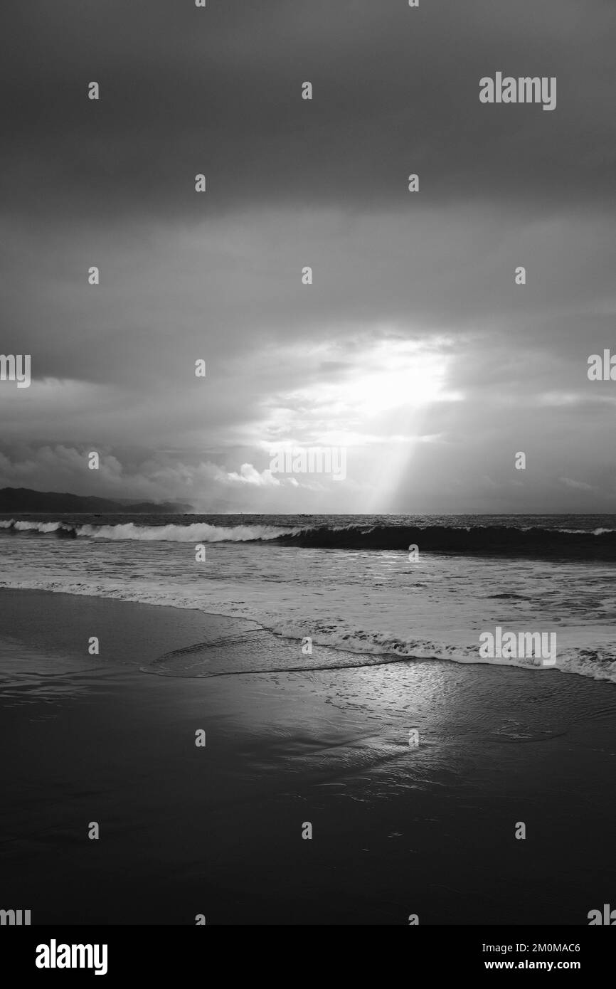 Photo en noir et blanc, photo monochrome du lever du soleil sur la plage traversant d'épais nuages Banque D'Images