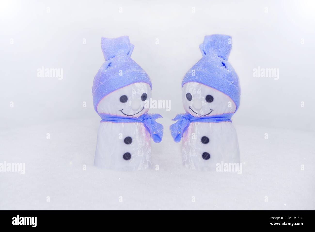 deux smowman debout sur la neige. jouet fait main avec chapeau et foulard en tissu bleu. flocons de neige - gros plan Banque D'Images