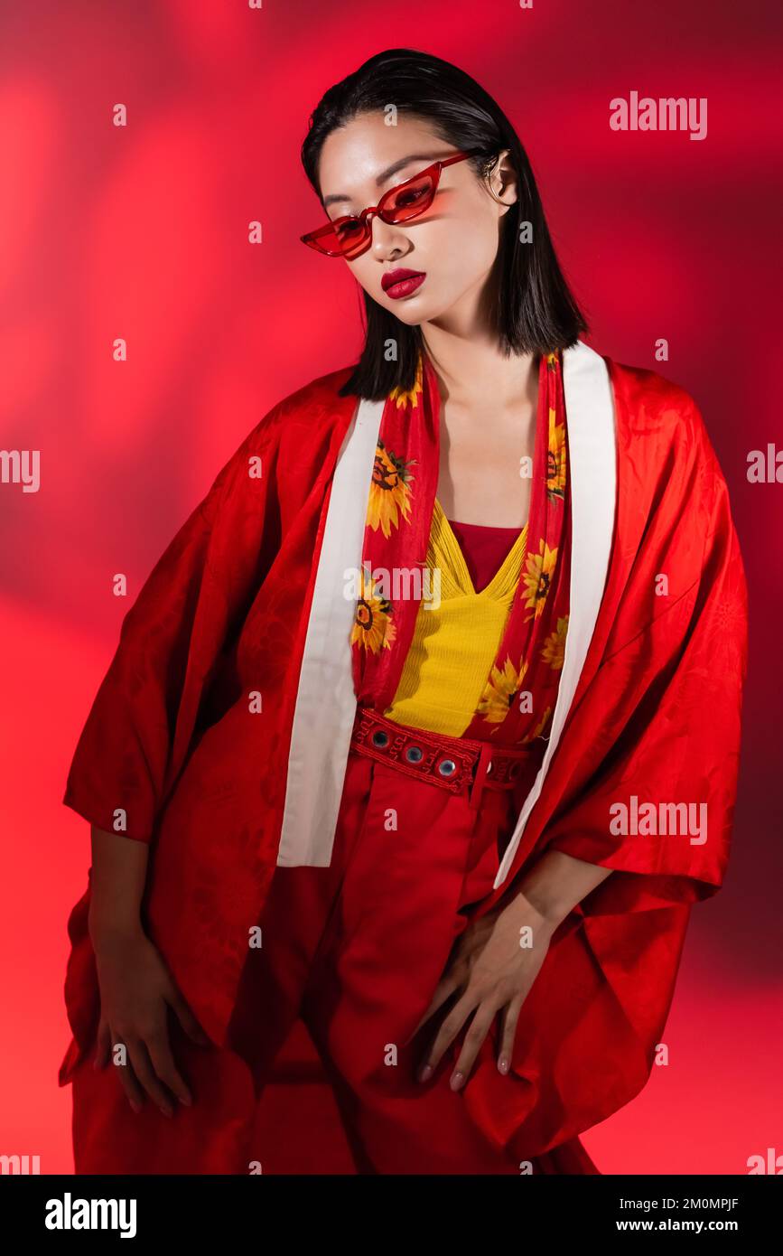 femme asiatique à la mode en kimono cape et lunettes de soleil posant sur  fond rouge avec ombre, image de stock Photo Stock - Alamy