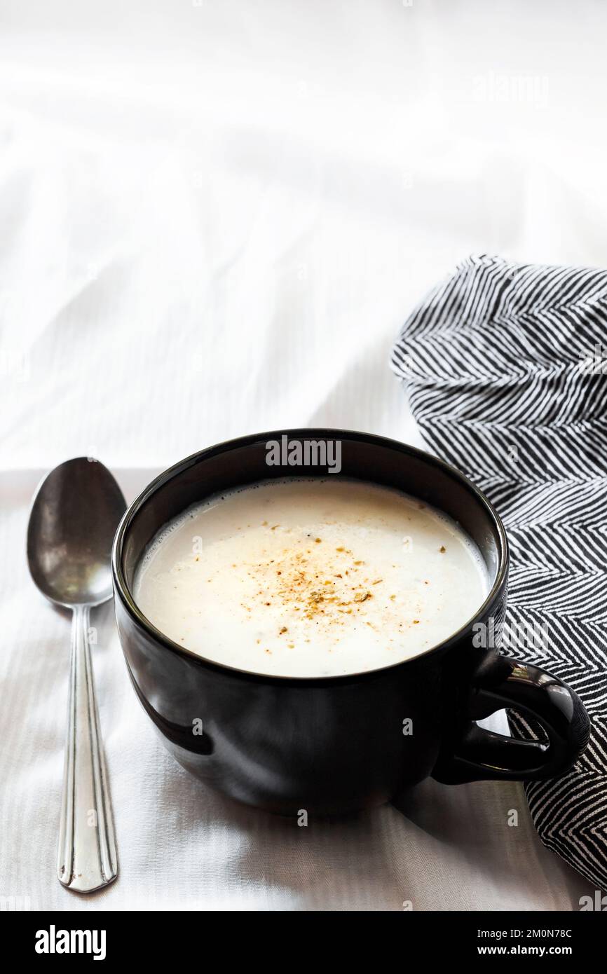Soupe de chou-fleur (crème du Barry) dans un bol noir sur fond blanc avec tissu noir et blanc. Banque D'Images Soupe de chou-fleur (crème du Barry) dans un bol noir sur fond blanc avec tissu noir et blanc. Banque D'Images