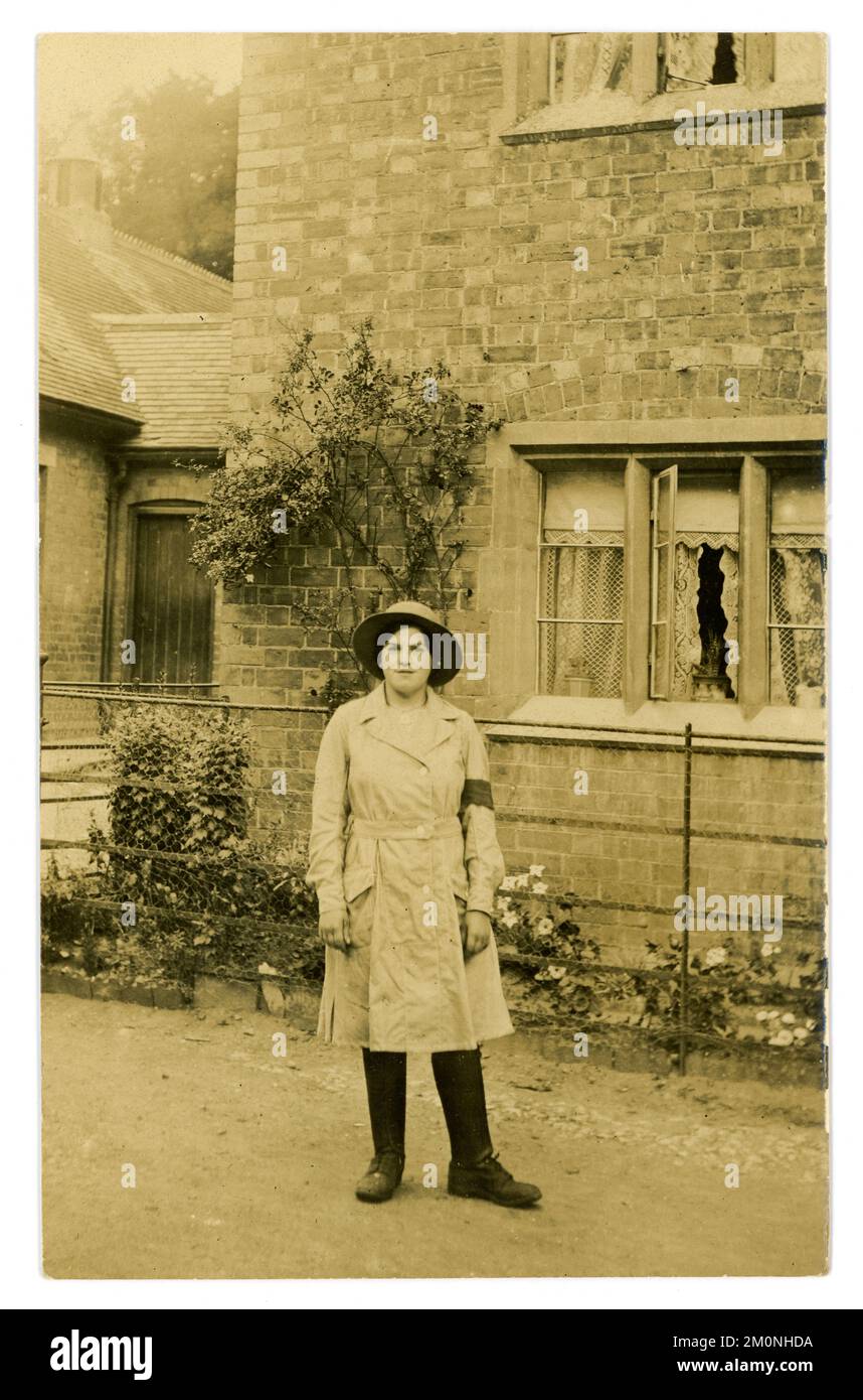 Carte postale originale de WW1 ans d'une jolie fille de terre debout à l'extérieur d'une maison de campagne portant un uniforme de culotte, chapeau de feutre, une tunique de longueur genou, (avec une ceinture intégrée à fermeture à bouton) bras, leggings en cuir et bottes, vers 1917, 1918 R.-U. Banque D'Images