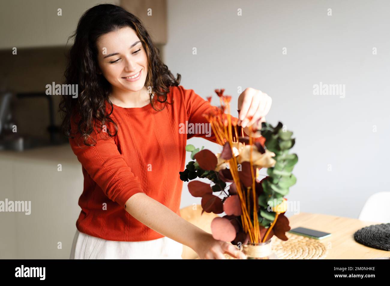 Jeune femme heureuse organisant des fleurs séchées dans un vase et plaçant la table dans la cuisine Banque D'Images