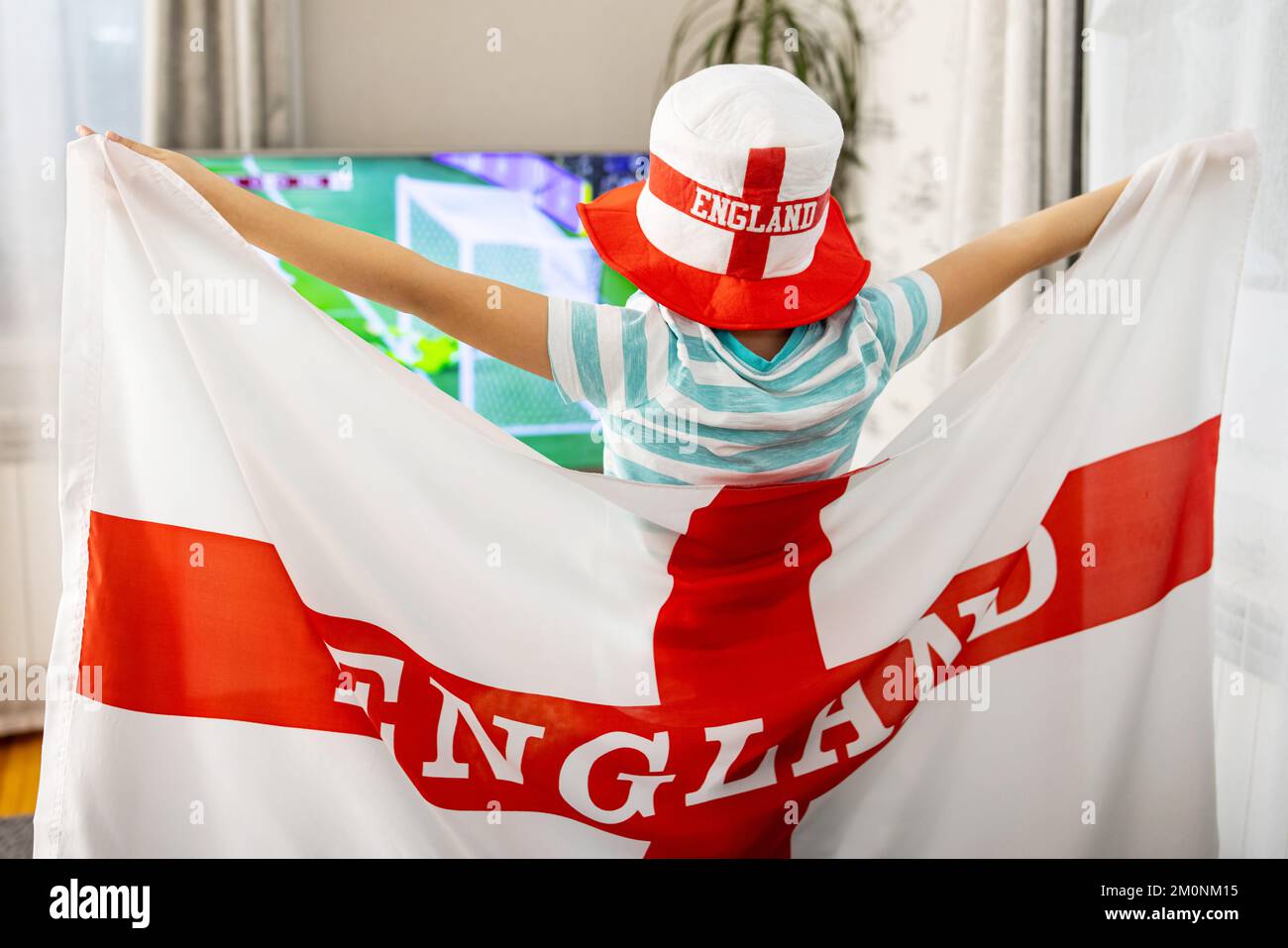 Un garçon tenant le drapeau de l'Angleterre et regardant un match de football à la télévision à la maison Banque D'Images