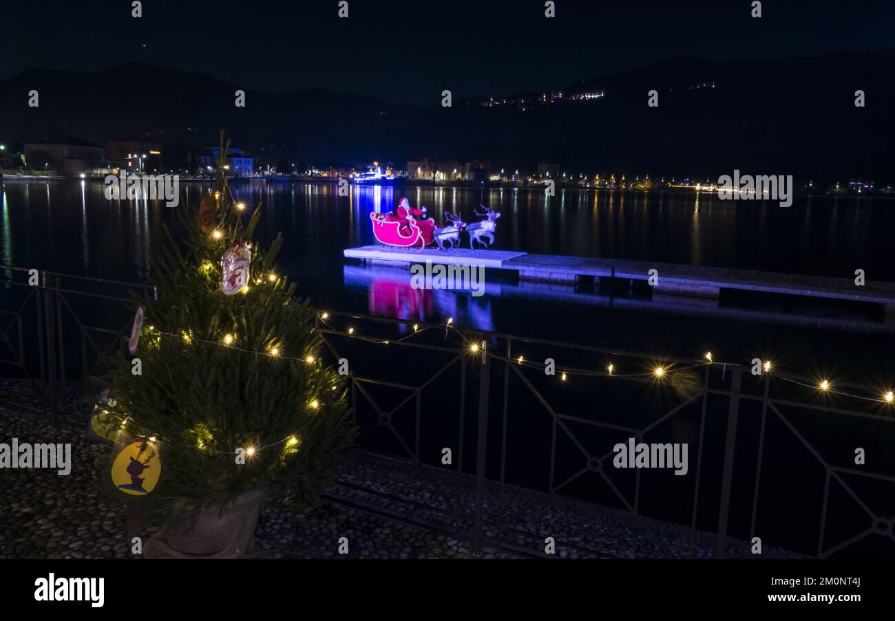 Porto Ceresio, Italie: 12-25-2021: Le Père Noël avec son traîneau et son renne illuminés se reflétant sur le lac de Lugano Banque D'Images
