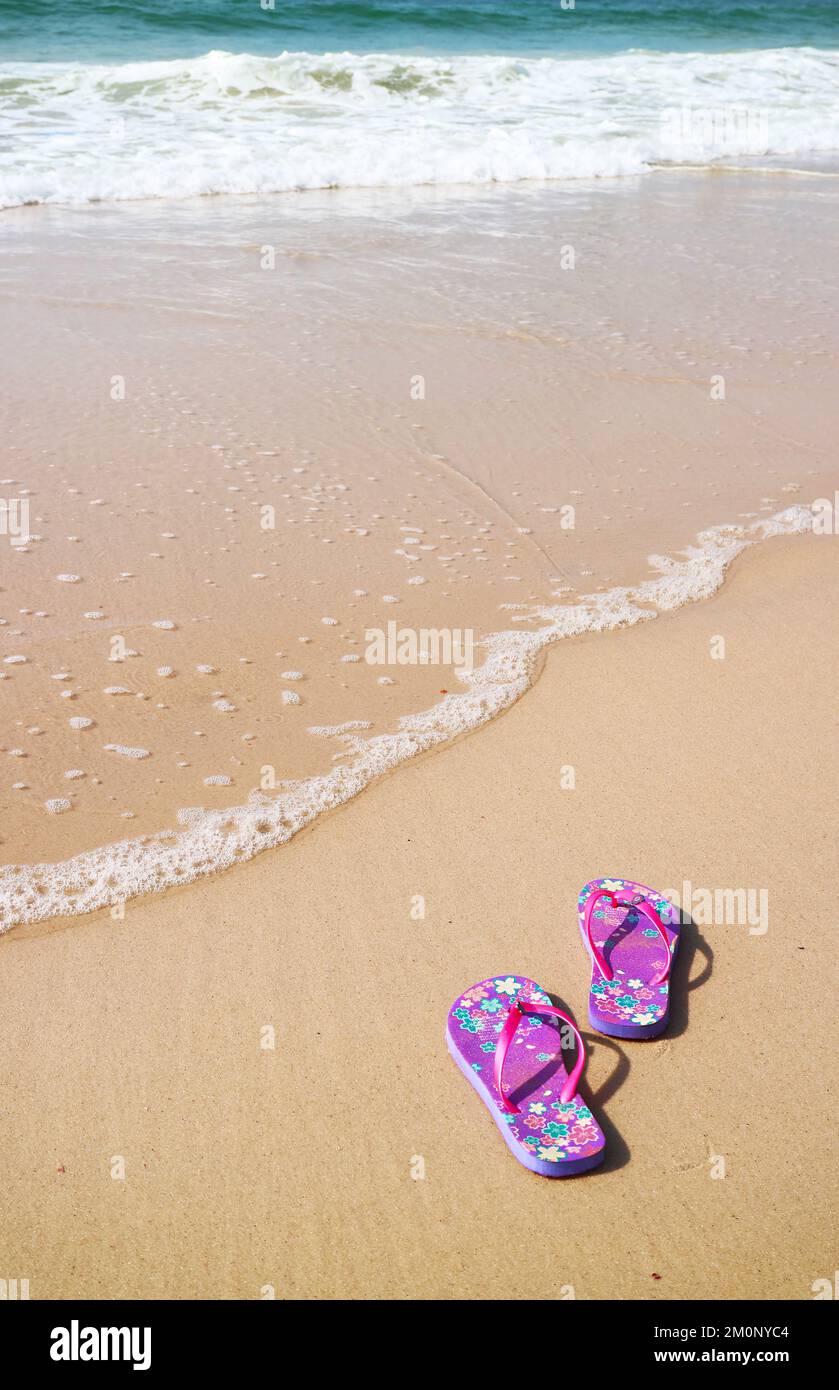 Une paire de sandales à tongs violettes sur la plage avec le lavage à l'arrière, plage de Copacabana, Brésil Banque D'Images