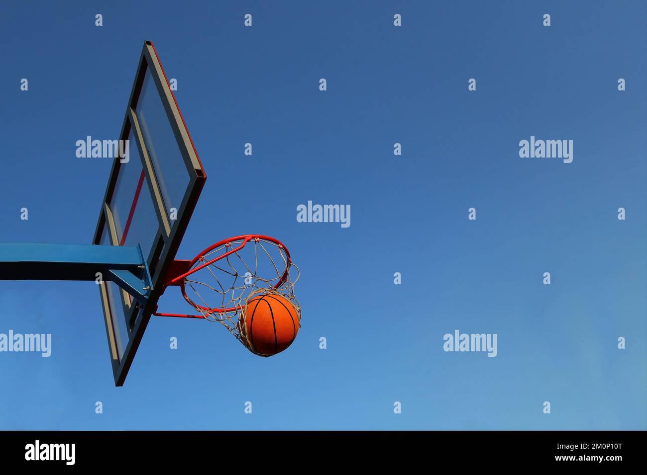 Un basket-ball dans un panier sur un terrain de basket-ball extérieur. Match de basket-ball, anneau et panier de basket-ball sur fond de ciel. Balle et panier contre le ciel dans le but. Banque D'Images