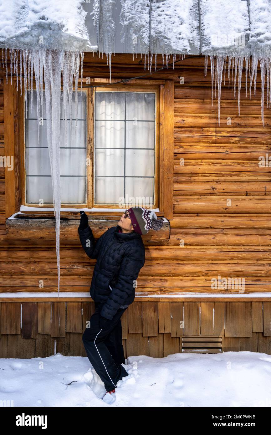 Femme regardant de longs glaçons suspendus sur un toit en métal à Wood Cabin Banque D'Images