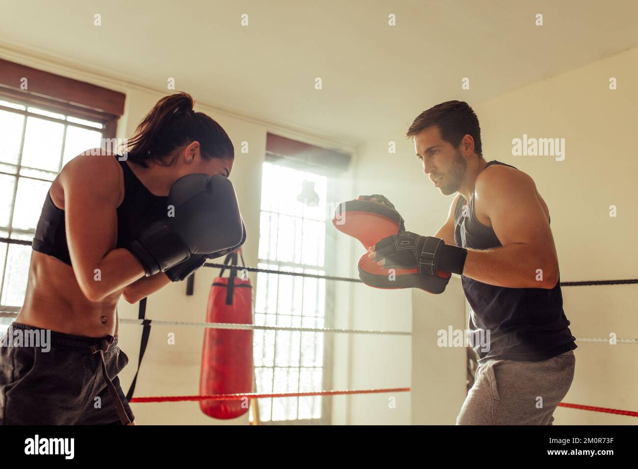 Des exercices pugilistes féminins avec instructeur dans l'anneau de boxe comme le soleil se met à travers deux grandes fenêtres Banque D'Images