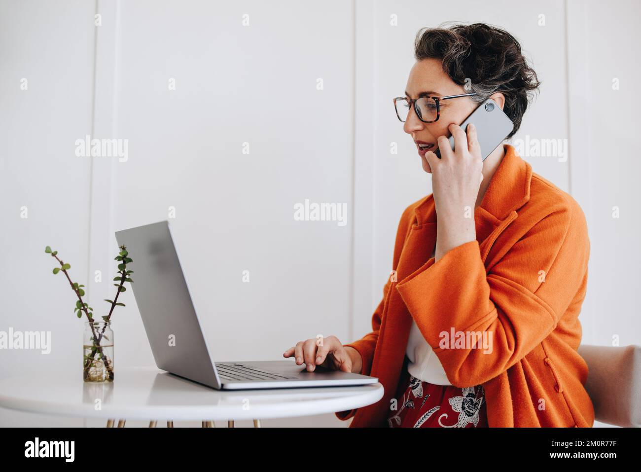 Femme d'affaires mature parlant au téléphone et utilisant un ordinateur portable tout en travaillant dans un café. femme d'affaires ayant une discussion téléphonique avec un client whi Banque D'Images