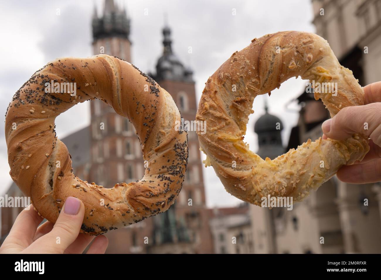 Femme touristique mangeant bagel obwarzanek cuisine polonaise traditionnelle en-cas en valant sur la place du marché St. Basilique Marie sur la place principale de Cracovie Rynek Glowny Pologne. Architecture de Cracovie, architecture de la vieille ville. Église catholique romaine historique à Cracovie Architecture baroque Voyages attraction touristique Banque D'Images