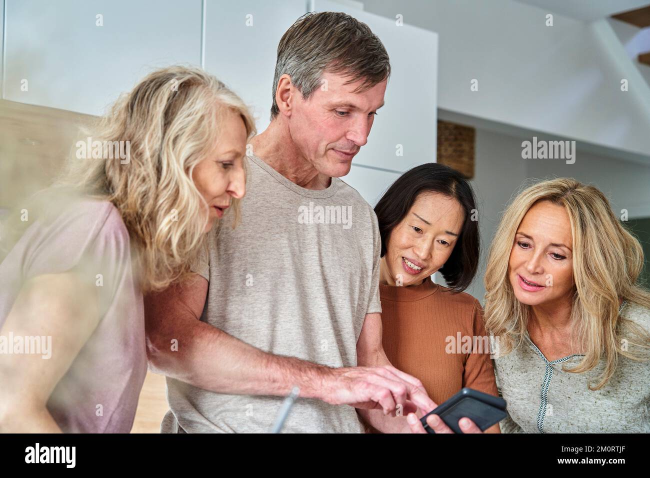 Groupe diversifié d'amis seniors utilisant le téléphone intelligent à la cuisine Banque D'Images