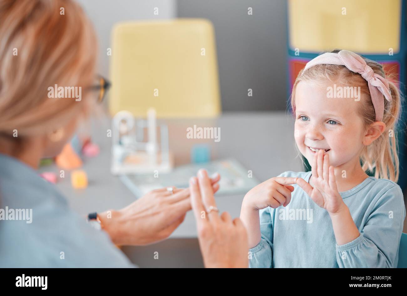 Adorable petite fille caucasienne souriante debout et utilisant le langage des signes pour communiquer avec un enfant psychologue dans une clinique. Professionnel de la santé mentale Banque D'Images