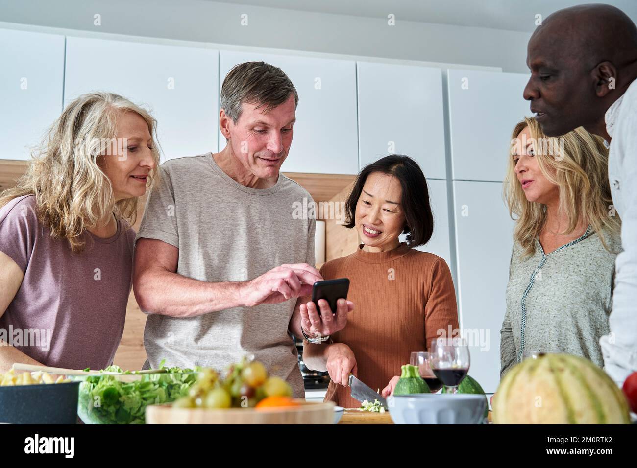 Homme senior à la recherche de recettes sur téléphone intelligent tout en se réunissant avec des amis Banque D'Images