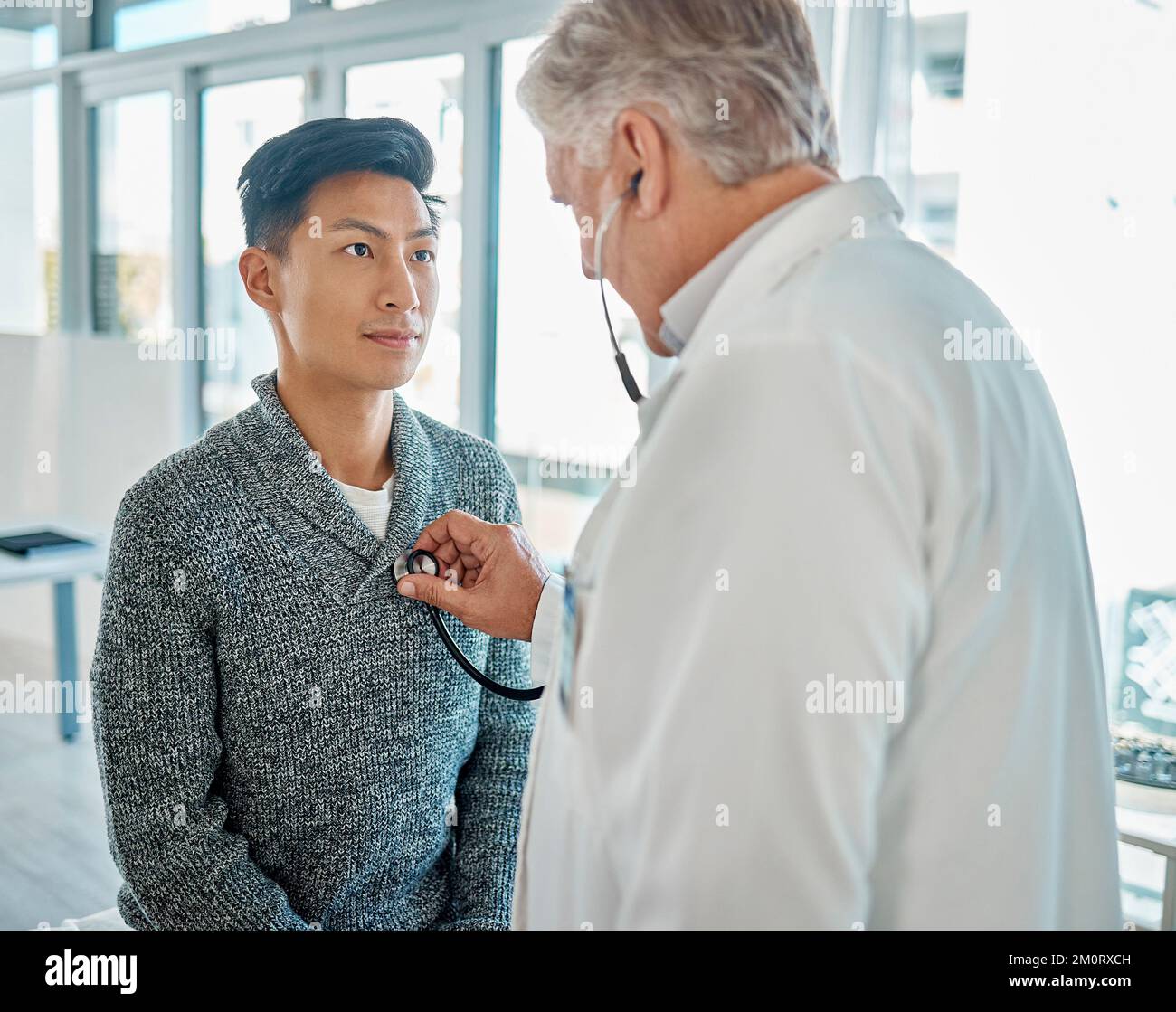 Homme asiatique faisant examiner sa poitrine et son cœur avec un stéthoscope par un médecin caucasien lors d'un examen médical de routine dans un hôpital ou une clinique Banque D'Images