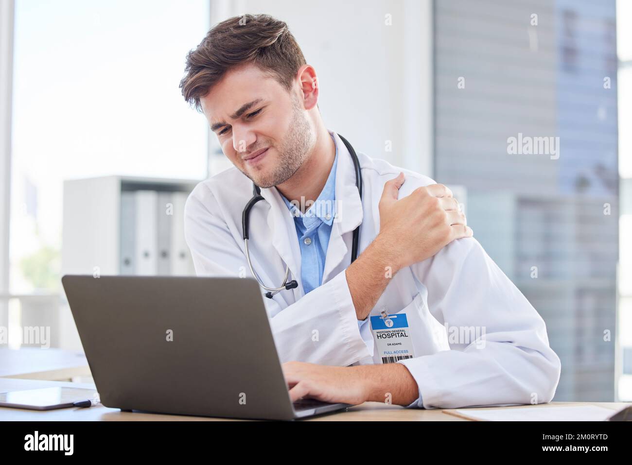Ordinateur portable, douleur d'épaule et soins de santé avec un médecin au travail dans son bureau à l'hôpital pour la recherche. Ordinateur, blessure et données avec un médicament Banque D'Images