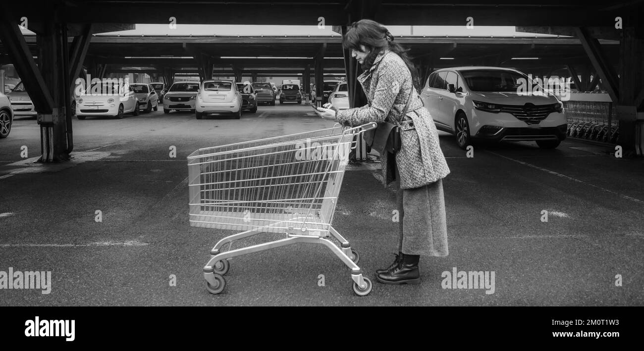 jeune femme hispanique adulte poussant le chariot lisant la liste de courses de smartphone dans le stationnement dans le grand magasin de supermarché Banque D'Images