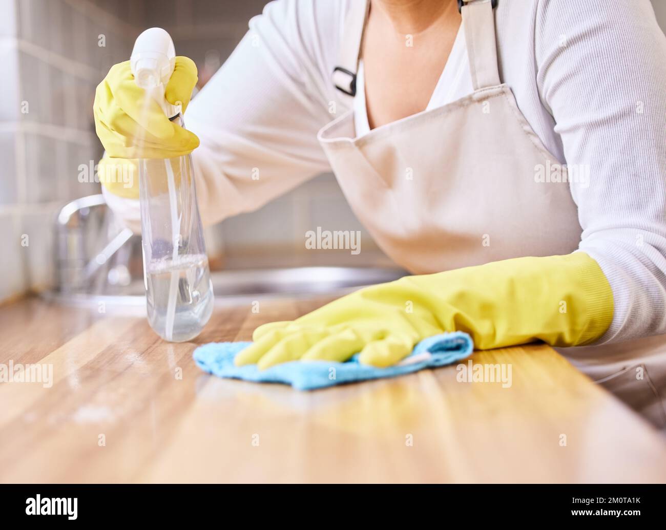 Main d'un nettoyant méconnaissable pulvérisant et essuyant une surface de table avec un chiffon propre seul à la maison. Une femme nettoyant un comptoir tout en portant Banque D'Images