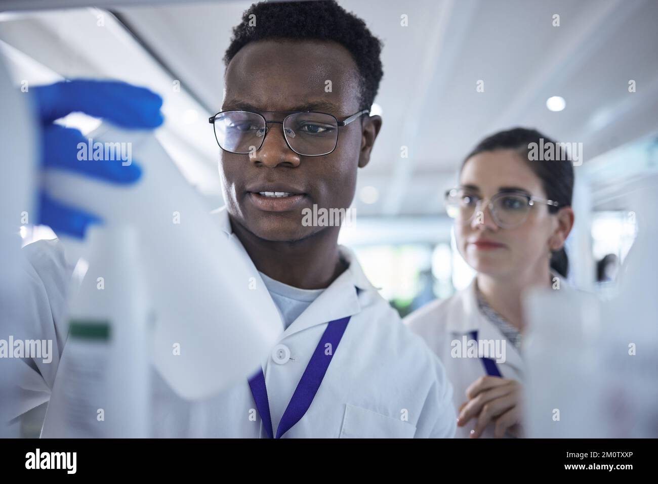 Un jeune scientifique afro-américain vérifie la bouteille d'échantillon avec une collègue féminine.deux professionnels de la santé travaillent ensemble sur des expériences en laboratoire Banque D'Images