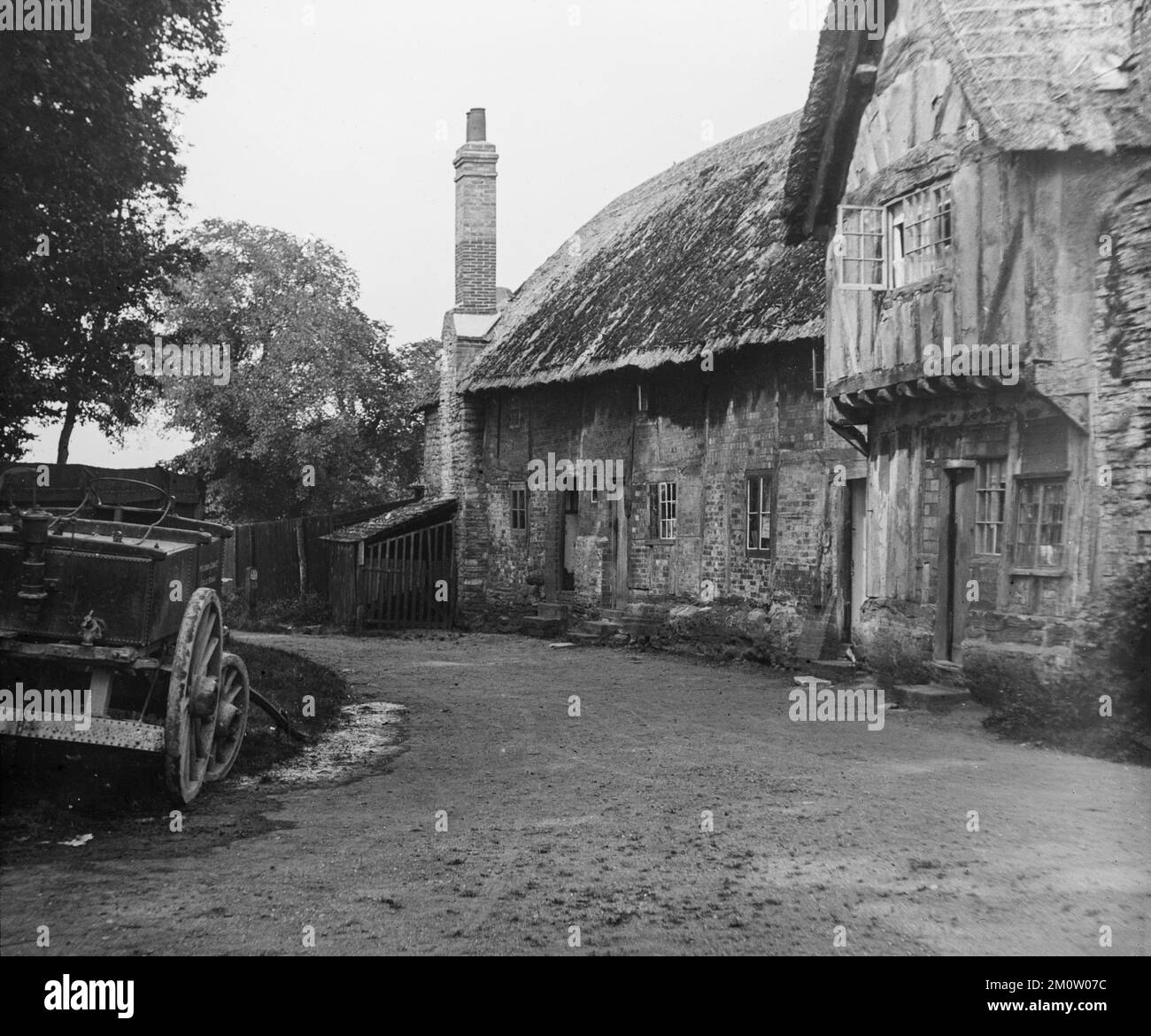 Une 19th photographie anglaise en noir et blanc de la fin du siècle montrant des cottages traditionnels en brique construits en chaume dans un village avec une voiturette à cheval à l'extérieur. Banque D'Images