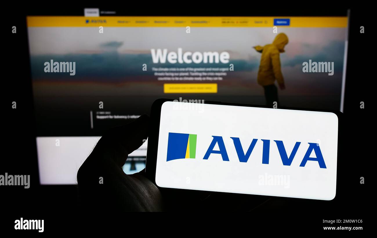 Personne tenant un téléphone portable avec le logo de la compagnie d'assurance britannique Aviva plc à l'écran en face de la page Web d'affaires. Mise au point sur l'affichage du téléphone. Banque D'Images
